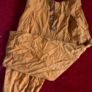 Gula linnebyxor från Pull&Bear - senapsgula baggy byxor av bomull och linne från Pull&Bear med hög midja och vida ben. gjorda för att sluta på smalbenet ungefär. har knappar framtill och är perfekta för varmare dagar. stl 32