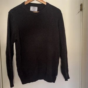 Mörkgrå stickad tröja från Kronstadt - Säljer en mörkgrå stickad tröja från Kronstadt med diskret sicksackmönster. Tröjan har rund halsringning, ribbade muddar och lång ärm. Perfekt för lager-på-lager och chill höst- eller vinterstil. Storlek:M! Pris kan diskuteras samt skriv till mig vid eventuella frågor🤩