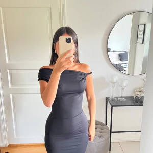 Svart offshoulder långklänning - Säljer en svart långklänning med offshoulder-design och figurnära passform. Klänningen har en stilren och enkel look, perfekt för dig som gillar minimalistisk stil. Materialet känns mjukt och stretchigt, vilket gör den bekväm att bära hela kvällen.Passar dig som har storlek 34 & 36!