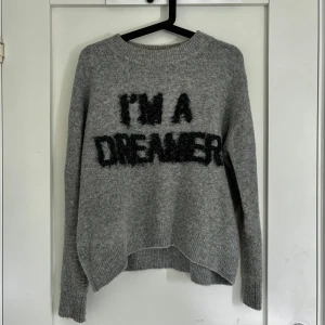 Grå stickad tröja med text - Mysig grå stickad tröja med svart fluffig text där det står 'I'M A DREAMER'. I jättefint skick, inte nopprig. Från H&M i storlek S.