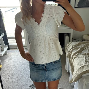 Vit spetsblus med volangärm - Superfin vit blus med broderade detaljer och spetskantad v-ringning. Blusen har korta volangärmar och ett luftigt, lätt utställt fall. Perfekt till jeans eller kjol för en romantisk look.