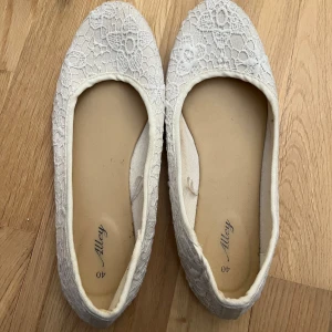 Vita spetsballerinaskor från Alley - Söta vita ballerinaskor från Alley i storlek 40. Skorna har ett romantiskt spetsmönster över hela ovandelen och rund tå. Perfekta för dig som gillar en feminin och stilren look. Platt sula för skön komfort hela dagen. Finns missfärgning på insidan och lite runt fotsulan på yttre, men annars relativt vit och fin 