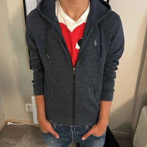 Mörkblå zip  från Ralph Lauren - Snygg mörkblå zip från Ralph Lauren med dragkedja och huva. Tröjan har långa ärmar, två fickor fram och den klassiska broderade loggan på bröstet. Perfekt för en chill och stilren look.