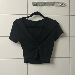 Svart omlottopp - Snygg svart topp med omlott-design och knyt framtill. Kortärmad och croppad modell med djup v-ringning, perfekt för en trendig look. Enkel att matcha med både jeans och kjol.