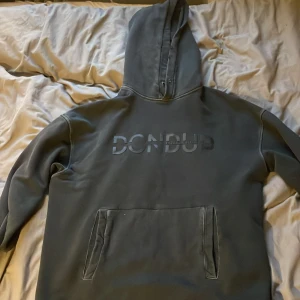Svart hoodie från Dondup med tryck - Snygg svart hoodie från Dondup med stort ton-i-ton tryck på bröstet. Klassisk känguruficka framtill och stor huva. Tillverkad i mjukt material, perfekt för chill eller streetwear. Made in Italy och riktigt clean look.
