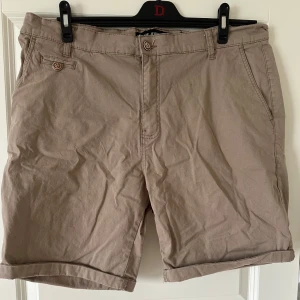 Beige shorts från Indigo Jeans 2XL - Snygga beige shorts från Indigo Jeans i storlek 2XL. Klassisk modell med knapp- och dragkedjestängning, bälteshällor och fickor både fram och bak. Perfekta för varma dagar och enkel att matcha med det mesta. Tillverkade i mjuk bomull för skön känsla.