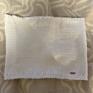 Vit bandeau tubtopp från hollister - Säljer en söt vit bandeau tubtopp från Bik Bok. Toppen är smockad med elastisk struktur och har volangkant upptill och nedtill. Perfekt för varma dagar och enkel att matcha med jeans eller kjol.
