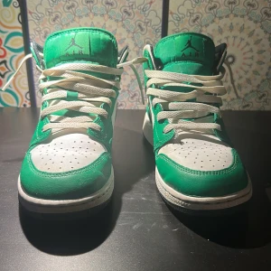 Nike Air Jordan 1 Mid Grön/Vit - Säljer ett par Nike Air Jordan 1 Mid i fräscha gröna och vita färger. Skorna har klassisk snörning, vit sula och svart innerfoder. Ikonisk Jordan-logga på sidan och tungan. Perfekta för dig som vill sticka ut med stilrena sneakers. Pytte lite creasade