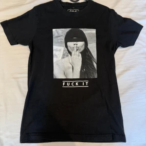 Svart t-shirt från Mister Tee med tryck - Svart t-shirt från Mister Tee i bomull med ett stort grafiskt tryck framtill som visar en person som kysser sitt långfinger och texten 'FUCK IT' under. Klassisk rund hals och korta ärmar. Perfekt för dig som gillar edgy streetstyle. Priset går självklart att diskuteras men tycker det är rätt eftersom tröjan är exklusiv. 😄