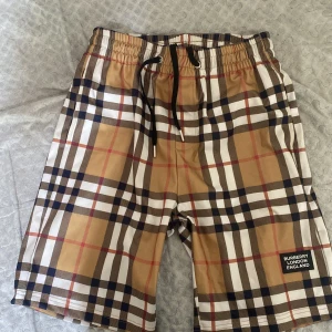 Burberry rutiga shorts med snörning - Snygga shorts från Burberry i klassiskt rutig design med beige, svart, vit och röda toner. De har elastisk midja med svart snörning och Burberry London England-märke på benet. Tillverkade i 100% bomull för en skön känsla. Perfekta för sommardagar när du vill sticka ut. Aldrig använt, fick den som present. pris kan diskuteras vid snabbaffär.