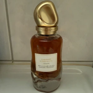 Donna Karan Cashmere & Palo Santo - 100ml, Cashmere & Palo Santo från Donna Karan är en lyxig parfym med träiga, vaniljiga och bärnstensnoter. Flaskan är elegant med en mjukt formad glasflaska och ett unikt, guldigt lock. Doften har inslag av mysk, balsam, pudriga och söta toner, perfekt för dig som gillar varma och mjuka dofter. Original pris ligger på 1,800kr