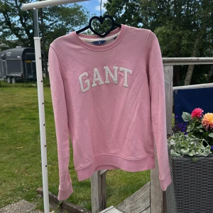 Rosa sweatshirt från GANT - Säljer en ljusrosa sweatshirt från GANT med broderad logga framtill. Tröjan har rund halsringning och långa ärmar. Tillverkad i mjuk bomull, perfekt för en chill och stilren look.