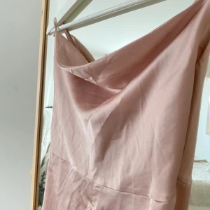 Ljusrosa långklänning från Boohoo - Säljer en ljusrosa långklänning från Boohoo i satinliknande material. Klänningen har smala axelband, draperad urringning och snygg snörning i ryggen. Perfekt för dig som vill ha en elegant och trendig look.
