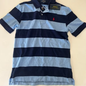 Blårandig Ralph Lauren piké - En fin ralph lauren piké till sommaren, i barnstorleken 14-16. I vuxenstorlek skulle jag säga att den ungefär motsvarar storleken S. Den är aldrig använd och har alla lappar kvar som det syns på bilden!