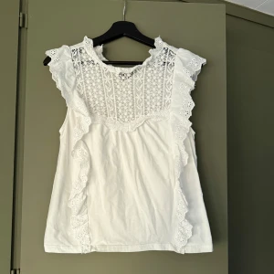 Vit spetsblus Mango  - Superfin vit blus från mango med broderade spetsdetaljer och volanger längs axlar och bröst. Perfekt till ett par linnebyxor nu i sommar. Köptes förra sommaren. 