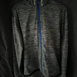 Träningskofta från H&M - Sportig gråmelerad vindjacka från H&M Sport med blå dragkedja och huva. Koftan har lång ärm, två fickor fram och är i fleece vilket även gör att den håller varmen ute. Perfekt för träning eller chill dagar ute.