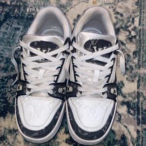 Louis Vuitton vita och svarta sneakers - Snygga Louis Vuitton sneakers i vitt och svart med tydliga LV-loggor på tungan, hälen och sulan. Dom är använda men inte jätte mycket nya går för mycket mer, säljs för att dom inte löngre passar.