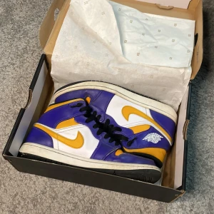 Nike Air Jordan 1 Lakers - Nike Air Jordan 1 sneakers i Lakers-inspirerad färg med lila, gult och vitt skinn. Klassisk high-top siluett med svart snörning, vit sula och ikoniska Jordan Wings-loggan på sidan. Perfekta för dig som vill sticka ut med färg och streetstyle. Storlek 40,5