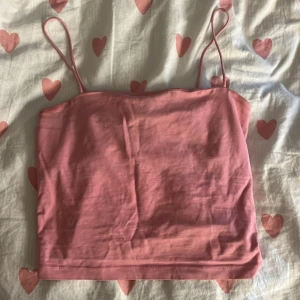 Rosa linnetopp från Gina Tricot - Säljer en söt rosa linnetopp från Gina Tricot med tunna axelband. Toppen är enkel och croppad i modellen, perfekt för varma dagar. Tillverkad i mjuk bomull som känns skön mot huden. Passar dig som gillar en stilren och chill look.