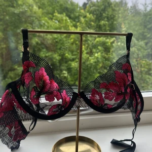 Blommig spets-bh från Bluebella - Supersnygg bh från Bluebella med transparent svart spets och stora broderade blommor i rosa och rött. Tunn mesh och fina detaljer gör den extra unik. ENBART testad och den passar inte mig!💕