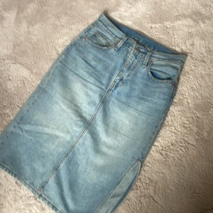 Ljusblå jeanskjol från Levi's - Säljer en snygg ljusblå jeanskjol från Levi's med klassiska fickor, bälteshällor och slit vid sidan.
