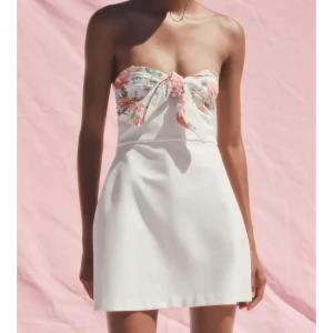Vit kort klänning med blommig topp - Superfin axelbandslös kort klänning i vitt med blommigt mönster och knyt framtill över bysten. Snygg och perfekt nu inför sommaren. Den är endast testad med prislapp kvar.