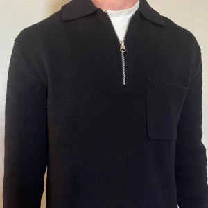 Blå stickad half zip-tröja Arket - Svart stickad tröja från Arket i storlek S passar även  M med krage, bröstficka och half zip-dragkedja. Klassisk och clean look med lång ärm, perfekt för lager-på-lager. Materialet är mjukt och värmande, passar dig som gillar stilren och enkel design.