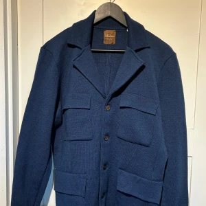 Blå overshirt från Stenströms, M - Snygg marinblå overshirt från Stenströms med fyra stora fickor framtill och klassisk krage. Overshirten är av merinoull och alpacka vilket ger ett mjukt material och stängs med pärlemoknappar. Perfekt lager-på-lager-plagg för dig som gillar stilren och avslappnad look. Overshirten är använd 1 gång och har sedan dess bara legat i garderoben vilket gör att den fortfarande är i nyskick. Nypris 3990kr, mitt pris 1200.