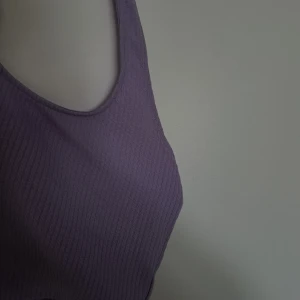 Ljuslila ribbad linnetopp Divided XS - Superfin ljuslila ribbad linnetopp från Divided H&M (Grekland) i storlek XS. Toppen är ärmlös med breda axelband och har en tight passform. Perfekt att styla med jeans eller kjol för en chill look. Materialet är mjukt och stretchigt för extra komfort.