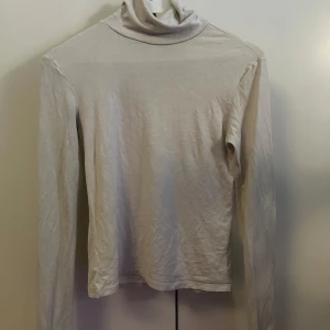 Beige polotröja från Gina Tricot - En stilren beige polotröja från Gina Tricot i mjuk bomull. Tröjan har lång ärm och klassisk polokrage, perfekt att styla med jeans eller kjol. Enkel och clean look som funkar året runt.