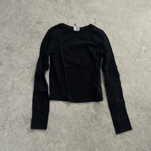 Svart långärmad topp från H&M Divided - En svart långärmad topp från H&M Divided, enkel och stilren med rund halsringning. Modellen är figurnära och passar perfekt till lager-på-lager eller som basplagg. Tillverkad i mjuk bomullsmix för en bekväm känsla hela dagen. Kortare passform, inte magtröja, ungefär till naveln på mig som är 169 cm. Inga defekter, men har blivit tvättad flertal gånger.