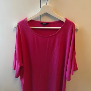 Ribbad rosa topp med öppna axlar - Rosa ribbad topp från Ellos med korta ärmar och öppna axlar. Toppens material är mjukt och stretchigt, perfekt för en chill och trendig look. Rund halsringning och avslappnad passform gör den enkel att styla till jeans eller kjol.