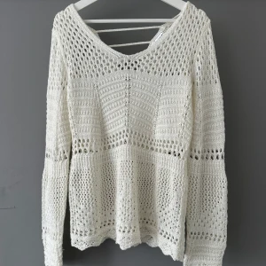Vit stickad tröja med hålmönster - Superfin vit stickad tröja med hålmönster och v-ringning. Tröjan har lång ärm och snygga virkade detaljer över hela plagget. Perfekt för lager-på-lager och ger en chill men ändå stilren vibe. Passar lika bra till jeans som till kjol.