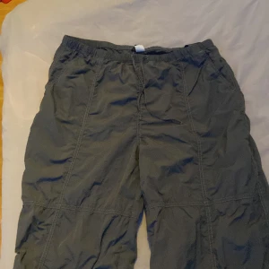 Mörkgrå cargo shorts med fickor - Säljer ett par mörkgrå cargo shorts med flera stora fickor och elastisk midja. Perfekta för dig som gillar en loose fit och praktiska detaljer. Materialet känns lätt och syntetiskt, vilket gör dem sköna under varma dagar.