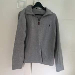 Grå half zip tröja från Ralph Lauren - Snygg grå långärmad tröja från Ralph Lauren med half zip och klassisk broderad logga på bröstet. Har en avslappnad passform med hög krage. Perfekt för lager-på-lager och chill vardagsstil. Storlek M.