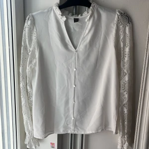Vit blus - Säljer denna vackra blus från SHEIN i storlek M. Den är i ett tunt och luftigt material som faller fint på kroppen och är perfekt för både vardag och fest. Blusen har romantiska spetsdetaljer längs ärmarna och axlarna, samt fina tygklädda knappar framtill som ger en elegant touch.