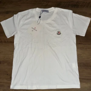 Vit Moncler t-shirt - Säljer en helt ny moncler tisha, på grund av att den är för liten. Moncler storlek 150 men passar som xs/mindre xxs.  Perfekt för dig som gillar stilrena och exklusiva plagg.