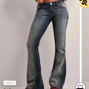 Blå bootcut jeans från True Religion - Snygga blå bootcut jeans från True Religion med klassisk femficksdesign och ikoniska bakfickor med kontrastsömmar. Jeansen har låg midja och är tillverkade i slitstarkt denim med lätt tvättad look. Perfekta för dig som gillar en retro vibe. Aldrig använda i storlek 27
