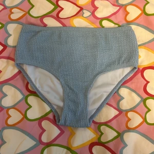 Blå bikiniunderdel från MIX Beachwear - Supersöt ljusblå bikiniunderdel från MIX Beachwear i storlek 146/152. Modellen är high waist och har en ribbad, smockad struktur som ger en trendig look. Perfekt för strandhäng och pooldagar. Materialet känns mjukt och följsamt mot huden.