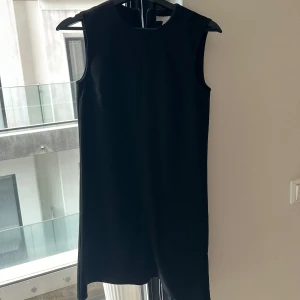 Svart ärmlös kortklänning - En stilren svart ärmlös klänning med rund halsringning och rak passform. Perfekt för dig som gillar minimalistisk och klassisk stil. Klänningen är enkel att styla med accessoarer och passar till många olika tillfällen.