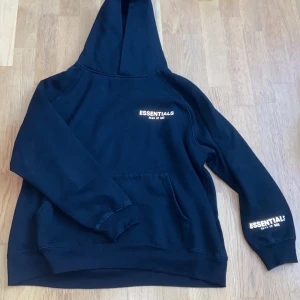 Essentials Fear of God Hoodie Svart - Svart hoodie från Essentials Fear of God i storlek M som är krympt lite för att den är tvättad flera gånger. Tillverkad i 100% bomull för en skön och avslappnad vibe. Priset kan diskuteras.