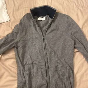 Grå kofta med dragkedja från Pier One storlek S - Snygg grå kofta från Pier One med hel dragkedja och ribbad krage. Tröjan har två fickor framtill och är tillverkad i mjuk bomullsmix. Perfekt för lager-på-lager och chill dagar. Enkel och stilren design som funkar till det mesta. Använd kanske 1-2 gånger men är för liten för mig. Storlek S