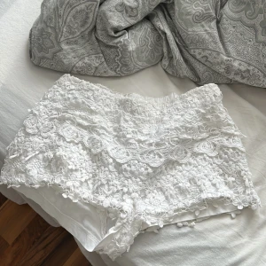 Vita spetsiga shorts med volang - Superfina vita shorts med spets och volangdetaljer. De har ett blommigt mönster i spetsen och är fodrade undertill för extra komfort. Perfekta för sommardagar när du vill ha en romantisk och söt look. helt som nya. Märket är borta så vet inte vart de ursprungligen kommer ifrån. 