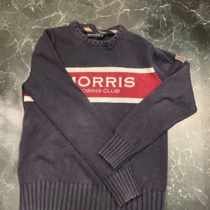 Morris tröja - Säljer en snygg mörkblå tröja från Morris med texten 'Morris Rowing Club' i rött och vitt på bröstet. Tröjan har långa ärmar och ribbade muddar vid ärmslut och nederkant. Perfekt för en stilren look!