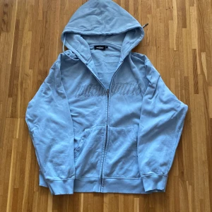 Ljusblå hoodie från Wasted - Säljer en ljusblå hoodie från Wasted med dragkedja och huva. Den har ett tryck på bröstet och är tillverkad i ett mjukt material. Perfekt för en avslappnad stil.