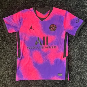 Rosa och lila PSG fotbollströja - Säljer en cool PSG fotbollströja i rosa och lila med korta ärmar. Tröjan har Jordan-logga och sponsortryck på framsidan samt spelarnamn och nummer 7 på baksidan. Perfekt för fotbollsfans!