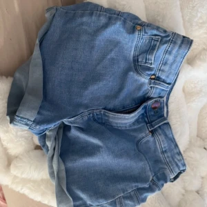 Blå jeansshorts - Snygga blå jeansshorts med klassisk design och upprullade kanter. Perfekta för sommardagar och avslappnade stunder. De har fickor både fram och bak samt en dragkedja framtill.
