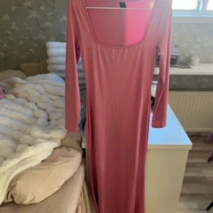 Rosa långklänning - Säljer en elegant rosa långklänning med långa ärmar och en fyrkantig urringning. Perfekt för en stilren look. Klänningen har en mjuk och bekväm passform.