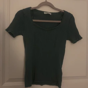 Grön ribbad topp från Holly & Whyte - Snygg grön ribbad topp från Holly & Whyte by Lindex. Toppen har korta ärmar och en rund halsringning med fina detaljer. FINNS TVÅ ANDRA LIKNANDE SOM LIGGER UPPE I ANDRA FÄRGER!!