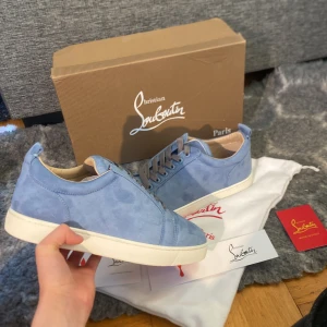 Blå sneakers från Christian Louboutin - Snygga blå sneakers från Christian Louboutin i mocka med klassisk röd sula. Skorna har grå snörning och en vit mellansula. Perfekta för att ge din outfit en lyxig touch. Vet ej om dom är äkta och tror inte de därav priset 